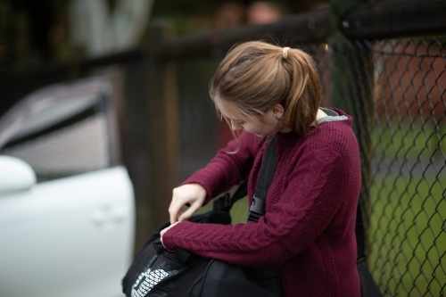 Teen girl zipping up duffel bag near car - Australian Stock Image