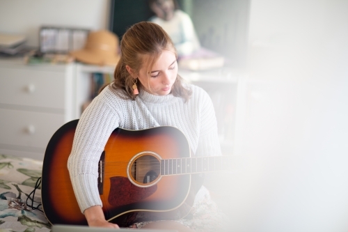 Teen learning guitar partly obscured by curtain