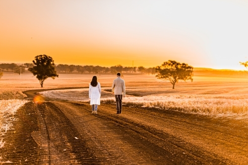 Teenage boy and girl walking together on rural dirt road at sunset - Australian Stock Image