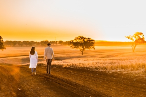 Teenage boy and girl walking together on rural dirt road at sunset