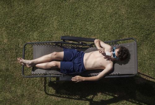 Teenage boy eating icypole while sunbaking - Australian Stock Image