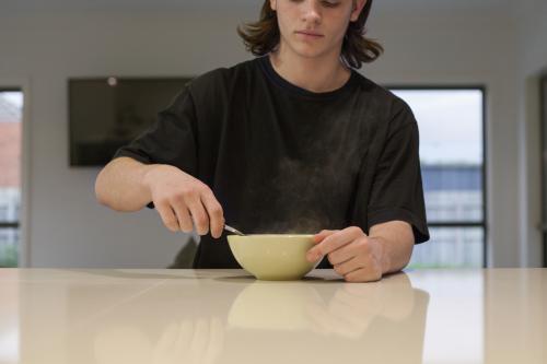Teenage boy eating noodles at a kitchen bench