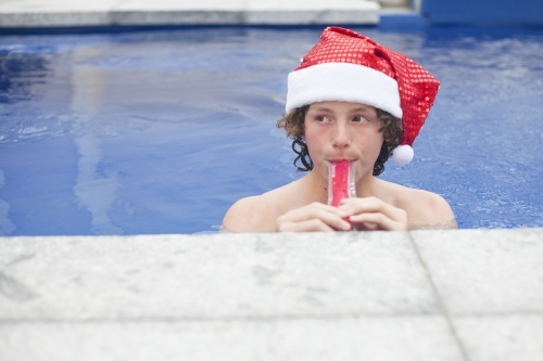 Teenage boy in Santa hat celebrating christmas in a pool - Australian Stock Image