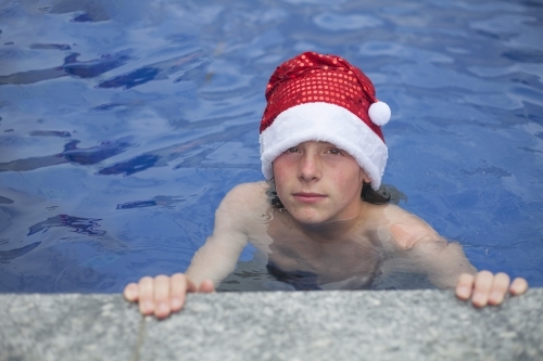 Teenage boy in Santa hat celebrating christmas in a pool - Australian Stock Image