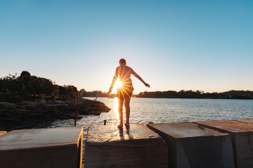 Teenage boy jumping from ledge into water in bright setting sun - Australian Stock Image