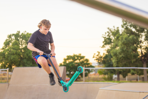 Teenage boy on scooter airborne on ramp at skate park - Australian Stock Image