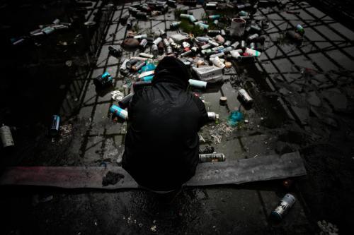 Teenage boy surrounded by empty spray cans in deserted warehouse - Australian Stock Image