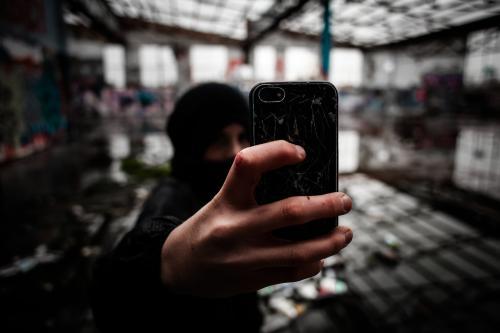 Teenage boy taking a picture on his mobile phone in deserted warehouse - Australian Stock Image