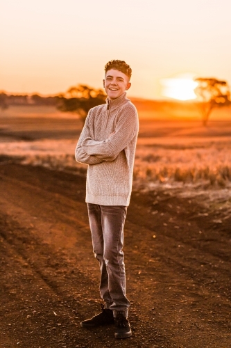 Teenage boy with folded arms on rural dirt road at sunset - Australian Stock Image