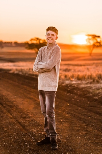 Teenage boy with folded arms on rural dirt road at sunset