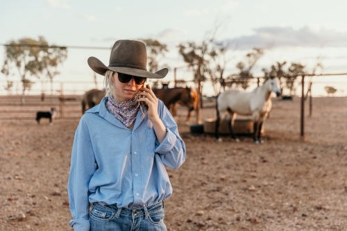 Teenage country woman on her phone standing in the horse yard - Australian Stock Image