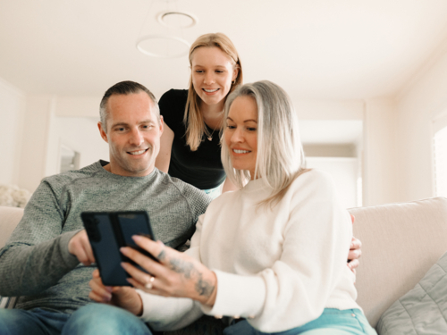 Teenage daughter leaning over her parents seated on the lounge looking at fold phone screen - Australian Stock Image