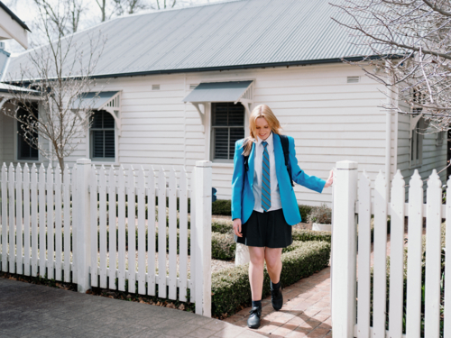 Teenage girl in blue uniform walking out of the picket fence of their new home - Australian Stock Image