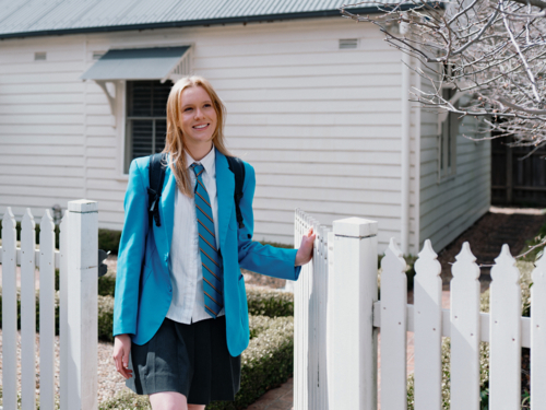 Teenage girl in blue uniform walking out of the picket fence of their new home - Australian Stock Image