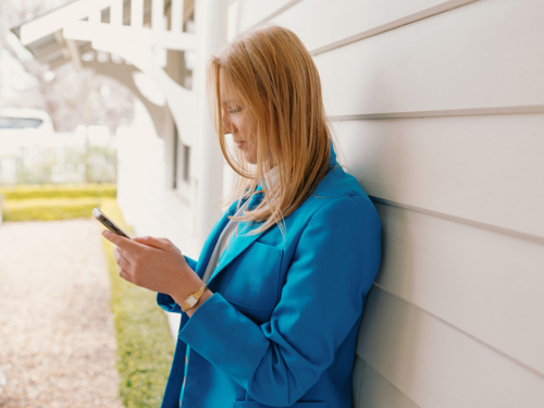 Teenage girl in school uniform leaning against the white wall while engaged on her phone - Australian Stock Image