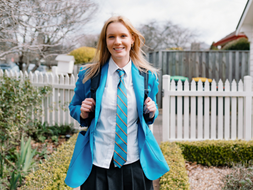 Teenage girl in school uniform stands along a curved brick path of their new home - Australian Stock Image