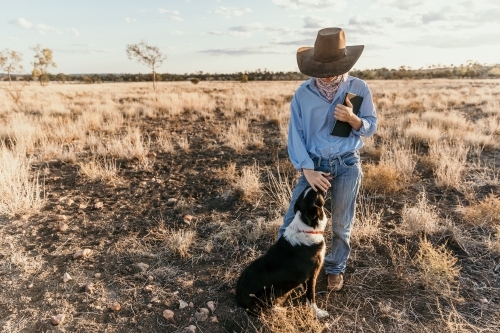 Teenage girl patting dog and holding her iPad in the paddock - Australian Stock Image
