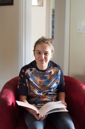 Teenage girl reading book in chair - Australian Stock Image