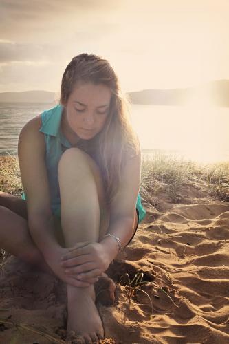 Teenage girl sitting on the beach at sunset - Australian Stock Image