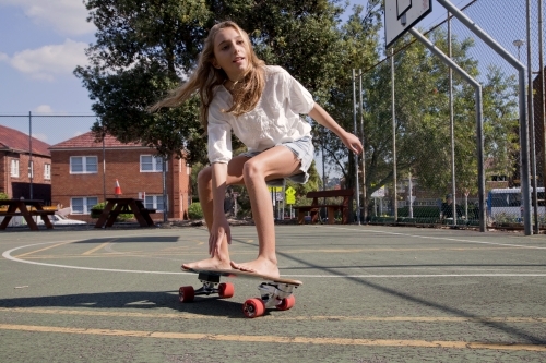 Teenage girl skateboarding in basketball court - Australian Stock Image