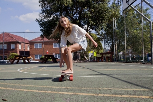 Teenage girl skateboarding in basketball court - Australian Stock Image