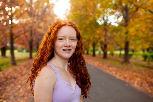 Teenage girl standing in a street lined with Autumn trees - Australian Stock Image