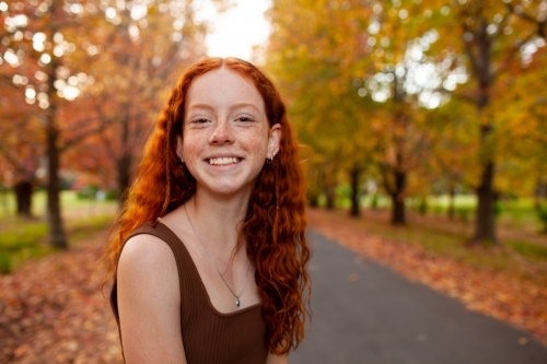 Teenage girl standing in a street lined with Autumn trees - Australian Stock Image