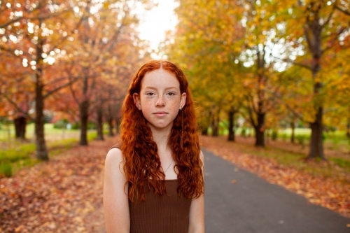Teenage girl standing in a street lined with Autumn trees - Australian Stock Image
