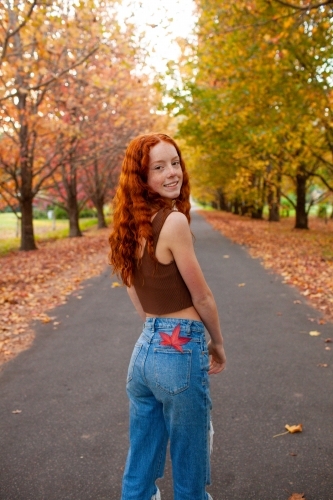Teenage girl standing in a street lined with Autumn trees - Australian Stock Image