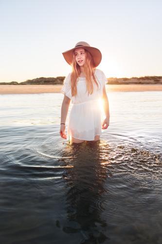 Teenage girl standing in calm water at the beach at sunset