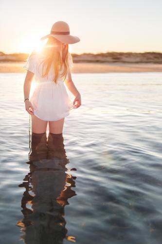 Teenage girl standing in calm water at the beach at sunset