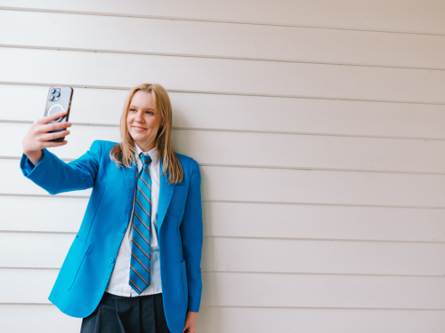 Teenage girl standing in front of white wooden wall taking a selfie - Australian Stock Image