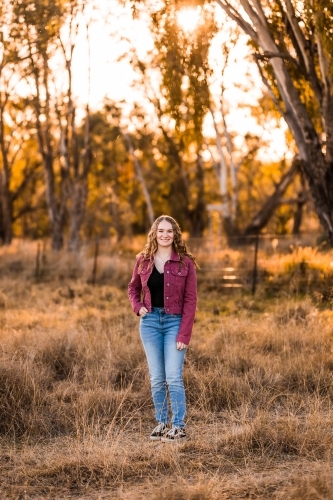 Teenage girl standing in long grass in paddock on farm - Australian Stock Image