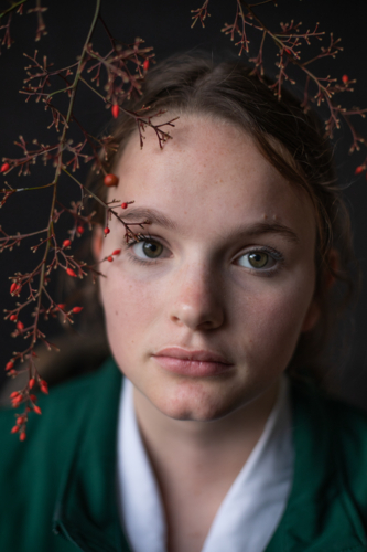 Teenage girl staring straight with red berries framing her face - Australian Stock Image