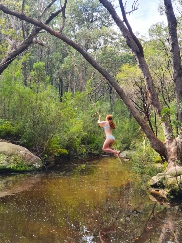 Teenage girl swinging on a rope swing at a rock pool - Australian Stock Image