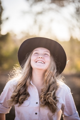 Teenage girl throwing head back laughing wearing akubra hat on farm in drought