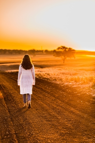 Teenage girl walking on dirt road at sunset - Australian Stock Image