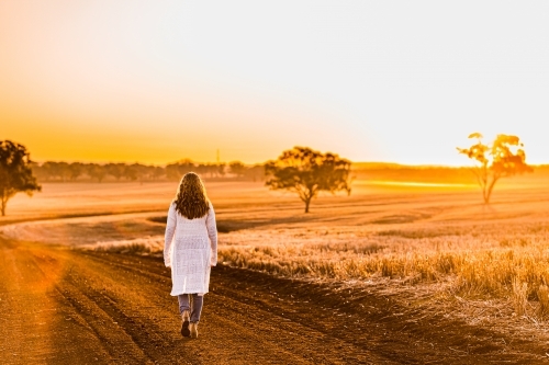 Teenage girl walking on dirt road at sunset - Australian Stock Image