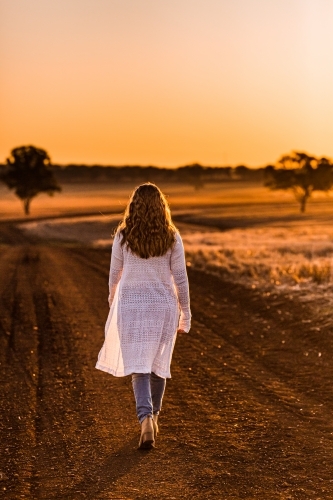 Teenage girl walking on dirt road at sunset - Australian Stock Image