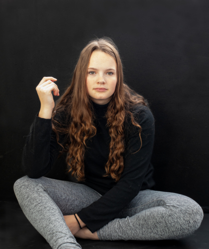 Teenage girl with long hair sitting on floor and looking at camera - Australian Stock Image