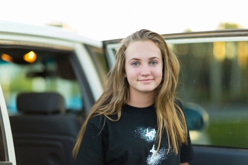 Teenage girl with long hair standing beside the car with open door - Australian Stock Image
