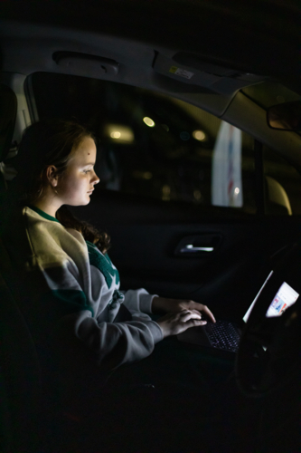 Teenage girl working on laptop in car at night - Australian Stock Image