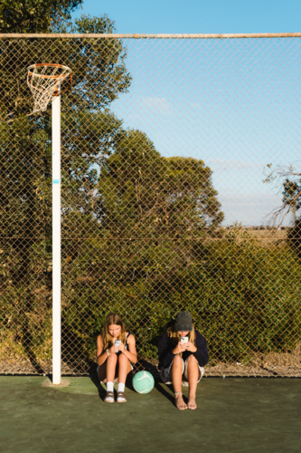 Teenage girls on phones at outdoor netball court - Australian Stock Image