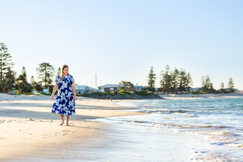 Teenaged Torres Strait Islander girl walking along coastal shoreline in traditional floral dress - Australian Stock Image