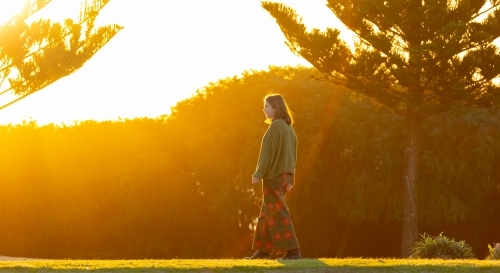 teenager back-lit walking past pine trees in coastal park - Australian Stock Image