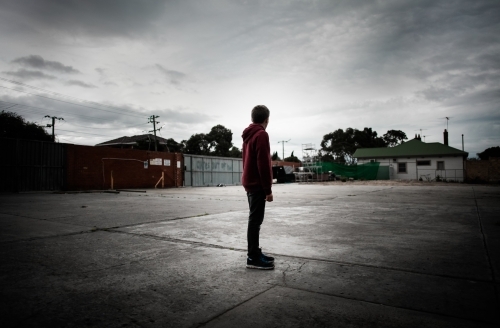 Teenager in a deserted parking lot looking into the distance - Australian Stock Image