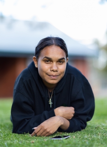 teenager wearing dark hoodie laying down on lawn - Australian Stock Image