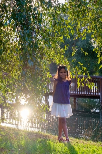 Ten year old girl standing on grass beside dam in park - Australian Stock Image