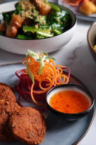 Thai fish cakes served on a plate with salad crunch and chili sauce on the side. - Australian Stock Image