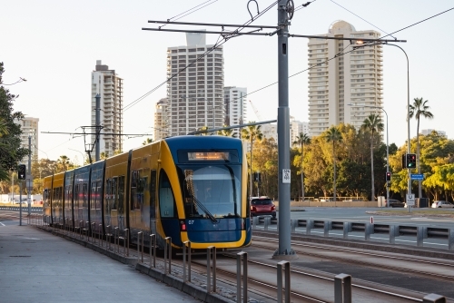 The G:link light rail tram on the Gold Coast passing station with Surfers Paradise buildings - Australian Stock Image